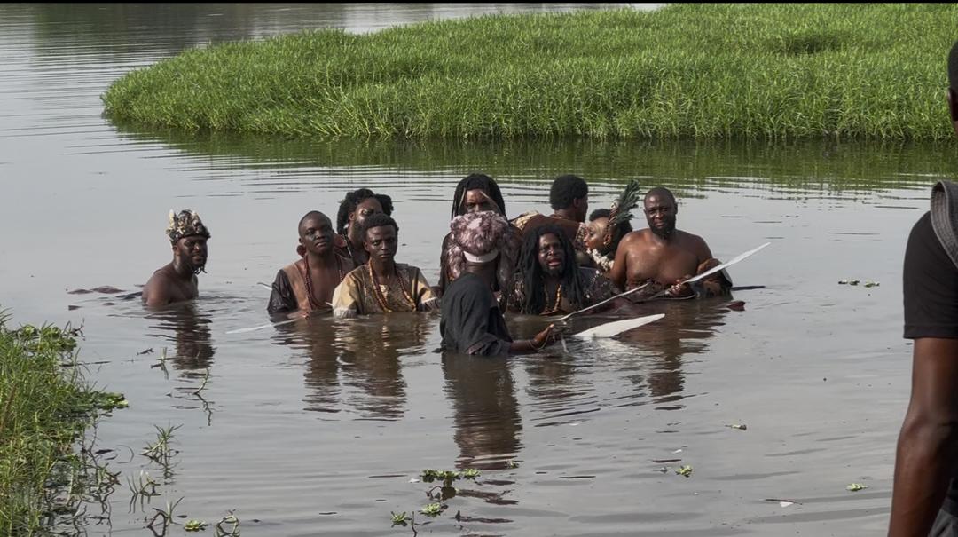 Warriors wading through the river during filming, holding paddles
