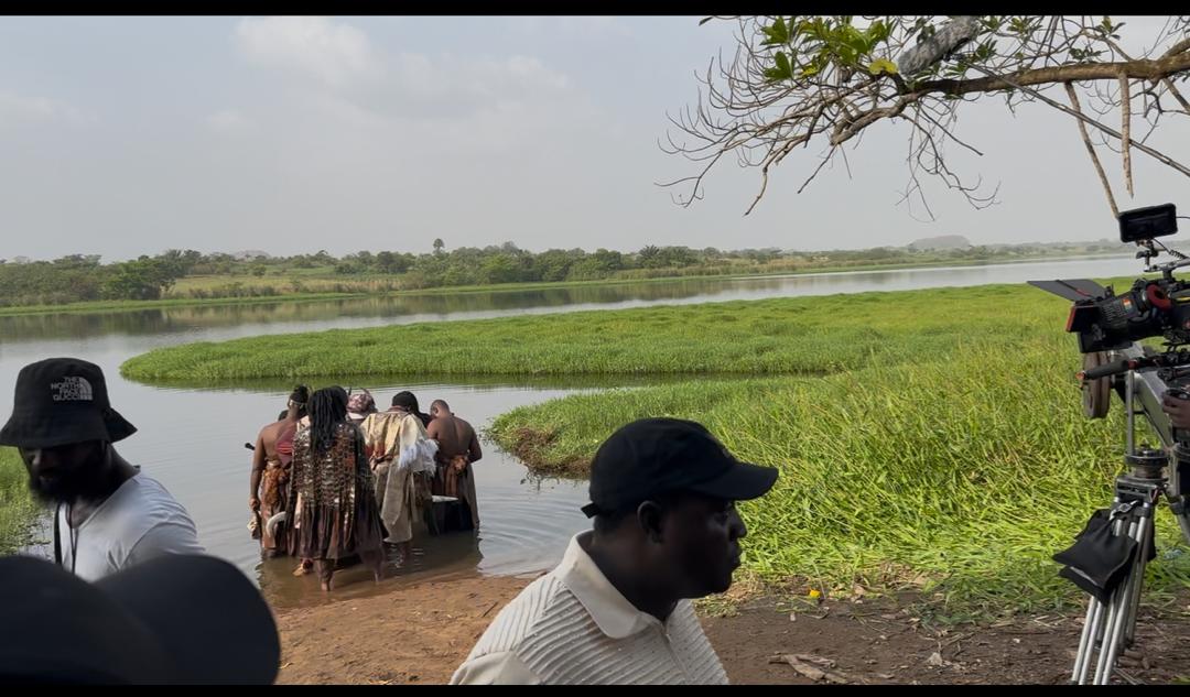 Wide shot of camera crew filming cast members at the riverbank